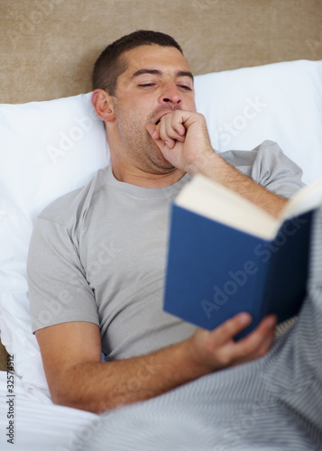 Foto: Young man yawning while reading book Young man yawning while reading book