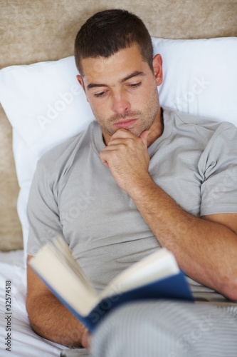 Photo: Handsome young guy reading book at home Handsome young guy reading book at home