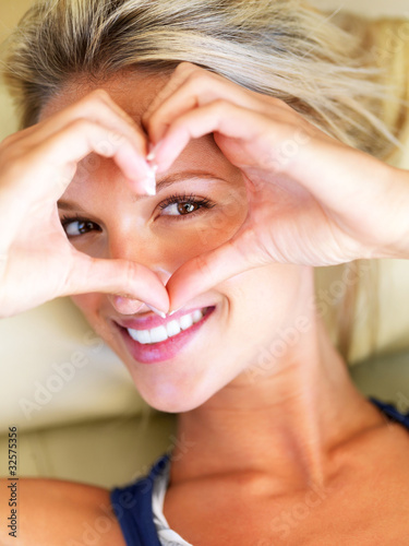 Photo: Beautiful woman looking through a heart sign Beautiful woman looking through a heart sign