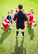 Rear view of a soccer coach in discussion with team on field