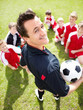 Happy coach looks at you with soccer team sitting on playground