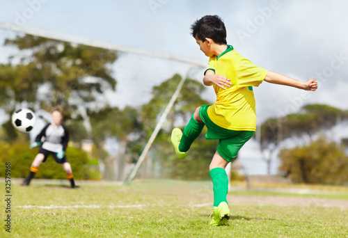 Photo: Young boy kicking football towards the goal at goal keeper Young boy kicking football towards the goal at goal keeper
