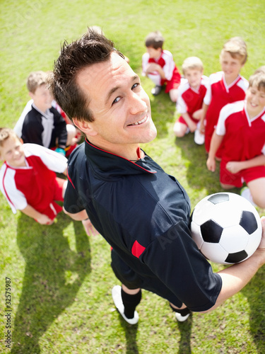 Photo: Happy coach looks at you with soccer team sitting on playground Happy coach looks at you with soccer team sitting on playground