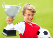 Soccer boy holding trophy and ball against green background
