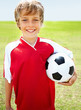 Confident smiling soccer kid holding a ball on field