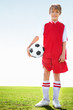 Happy soccer player holding ball on grass against sky