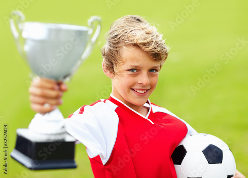 Photo: Soccer boy holding trophy and ball against green background Soccer boy holding trophy and ball against green background