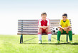 Two smiling rival players sitting with a soccer ball on bench