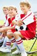 Happy soccer kids dressed in red sitting on a bench