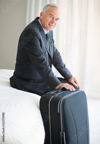 Foto: Happy senior man sitting on bed with his luggage Happy senior man sitting on bed with his luggage
