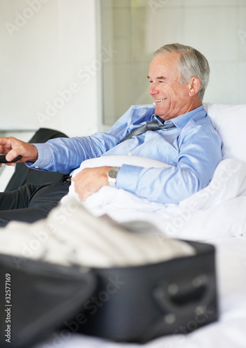 Foto: Mature business man with a remote control watching television Mature business man with a remote control watching television