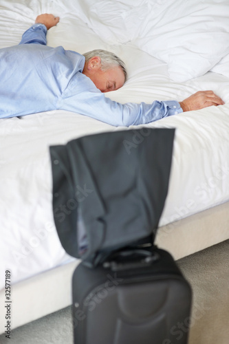 Photo: Exhausted matured man lying in bed at hotel Exhausted matured man lying in bed at hotel