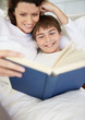 Happy young boy with his mother reading book in bed