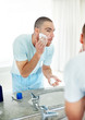 Reflection of man in bathroom mirror applying shaving cream