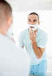 Reflection of man in bathroom mirror applying shaving cream