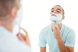 Middle aged man looking at mirror and shaving his beard