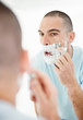 Middle aged man looking at mirror and shaving his beard