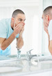Middle aged man looking at mirror while washing his face