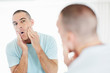 Middle aged man looking at mirror applying after shave lotion