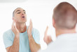 Blurred man looking at mirror uses a lotion after shaving