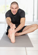 Happy middle aged male stretching his leg while sitting on mat