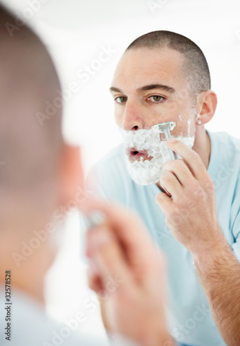 Photo: Middle aged man looking at mirror and shaving his beard Middle aged man looking at mirror and shaving his beard