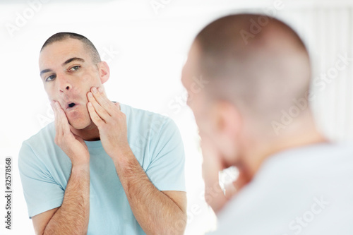 Photo: Middle aged man looking at mirror applying after shave lotion Middle aged man looking at mirror applying after shave lotion