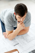 Young male architect looking at blue prints and drawing
