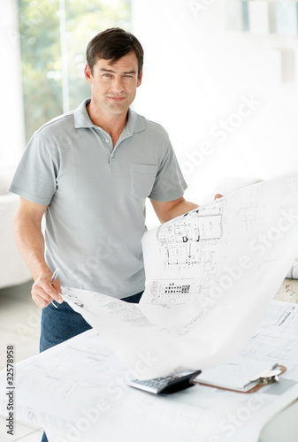 Photo: Happy young man standing in office and holding blue print Happy young man standing in office and holding blue print