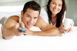 Guy lying on bed and watching television with his wife