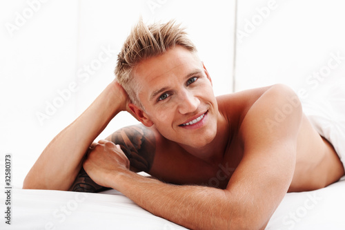 Foto: Young man relaxing in bed and smiling Young man relaxing in bed and smiling