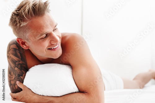 Foto: Man in bed cuddling his pillow and smiling Man in bed cuddling his pillow and smiling