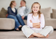 Girl sitting with hands folded and parentss in blur background