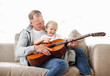 Happy boy playing guitar with his father while sitting in sofa