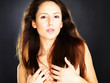Naked young woman covering her breast against dark background