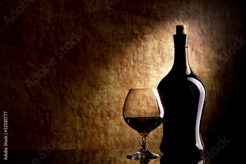 Photo: Cognac Glass and Bottle on a old stone background Cognac Glass and Bottle on a old stone background