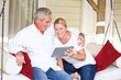 Mature couple with tablet computer in hanging lounger on veranda
