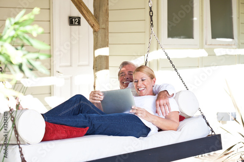 Photo: Mature couple with tablet computer in hanging lounger on veranda Mature couple with tablet computer in hanging lounger on veranda