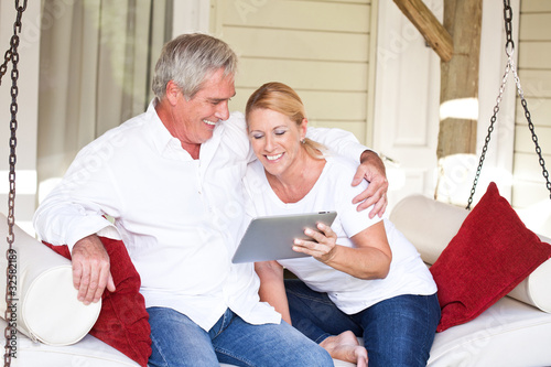 Photo: Mature couple with tablet computer in hanging lounger on veranda Mature couple with tablet computer in hanging lounger on veranda