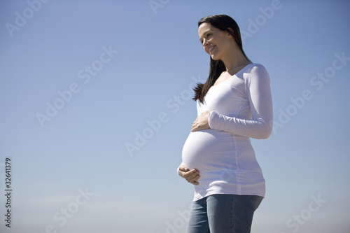Photo: A pregnant woman standing on the beach, holding her belly A pregnant woman standing on the beach, holding her belly