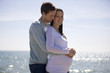 A pregnant woman and her partner embracing on the beach
