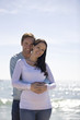 A pregnant woman and her partner embracing on the beach