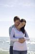 A pregnant woman and her partner embracing on the beach