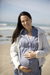A pregnant woman standing on the beach, smiling
