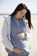 A pregnant woman standing on the beach, smiling