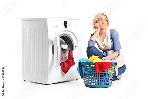 Photo: Woman in thoughts with clothes seated next to a washing machine Woman in thoughts with clothes seated next to a washing machine