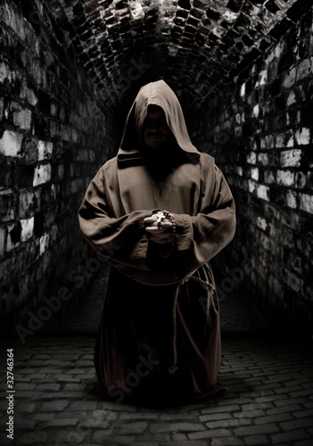 Photo: Praying monk in dark temple corridor Praying monk in dark temple corridor