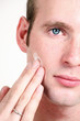 Close-up portrait of young handsome man applying face cream