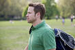 A young man walking through a park, carrying a sports bag