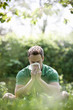 A young man sitting on the grass, blowing his nose